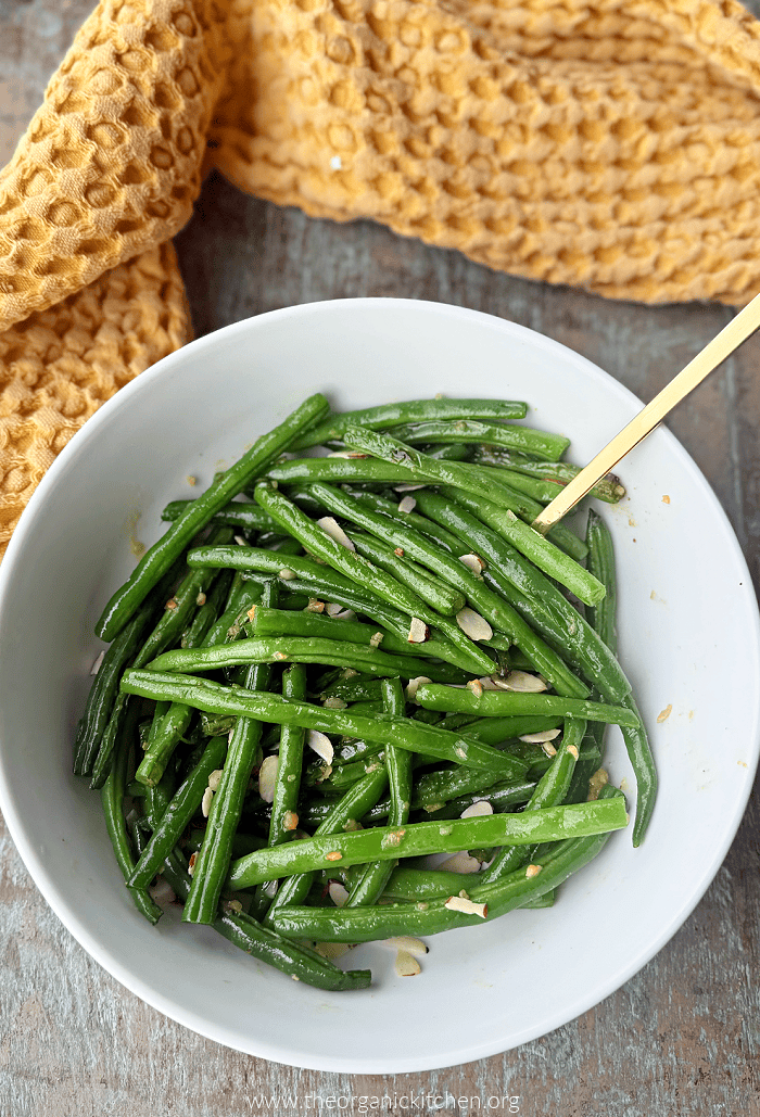 Copycat Din Tai Fung Green Beans garnished with sliced almonds in white bowl with gold spoon 
