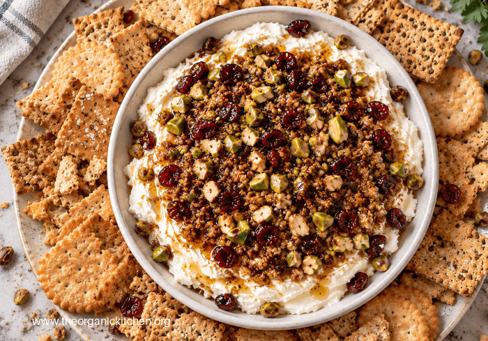 Whipped Cream Cheese with Warm Cranberries Whipped Cream Cheese with Warm Cranberries with pistachios in a hwite bowl surrounded by crackers